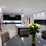 Monochrome black and white handless kitchen design detailing a stainless steel handle trim boasting a striking wine bottle holder feature wall illuminated by LED mood lighting.