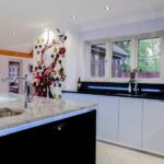 Modern handless black gloss island with prep sink and instant hot, chilled and sparkling water tap with contrasting white gloss handless units on main kitchen run.