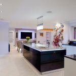 Two tone gloss handless kitchen with stainless steel trim, complimented by black granite worktop and upstands, with a contrasting marble effect quartz worktop on the island giving the ultimate show factor.