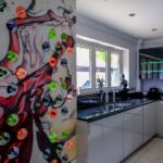 Bespoke one of wine bottle holder feature wall situated in a stylish modern white gloss handless kitchen complimented with black granite worktop and smoked glass LED illuminated wall units.