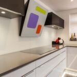 Two tone pearl grey and polar white gloss kitchen units with high end Miele integrated appliances in white. Wall mounted extractor hood above Miele induction hob.