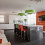 Modern gloss kitchen accessorised with pops of colours on soft furnishings while dominated by the bold orange glass accent wall.