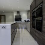 Open plan kitchen dinner fitted with a modern handless matt cashmere and wood effect door comination. Paired with white sparkle quartz worktop, upstand, and matching windowcill.